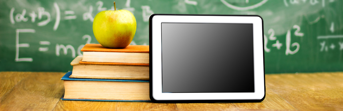 Green apple on 3 books next to a tablet in front of a chalk board